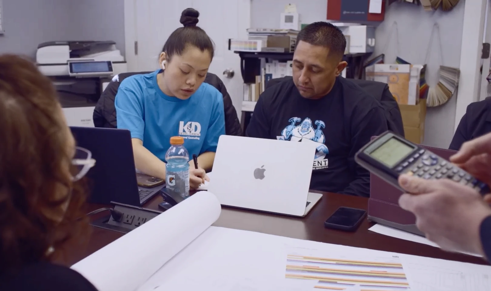 K&D Development team reviewing project documents and blueprints manually with laptops and calculators before adopting Vibe Board