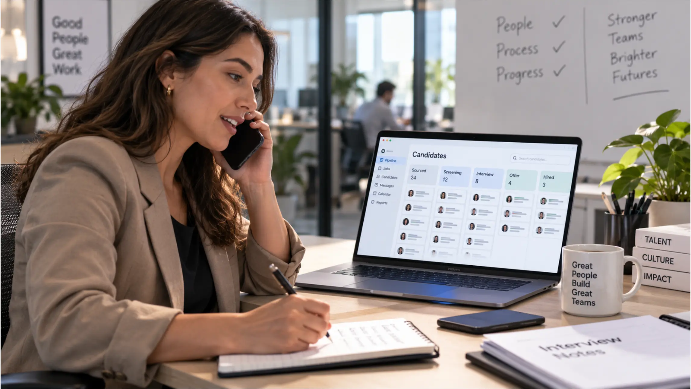 A recruiter at a desk with a phone and laptop, candidate pipeline visible on screen