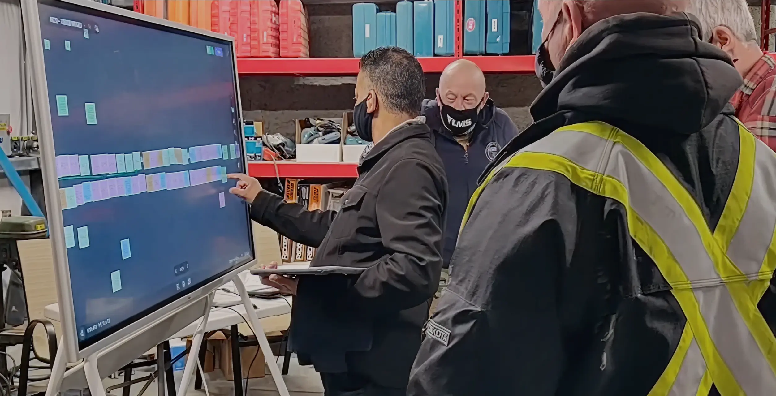 Construction team in safety vests reviewing a site logistics plan on a Vibe Board in a warehouse setting