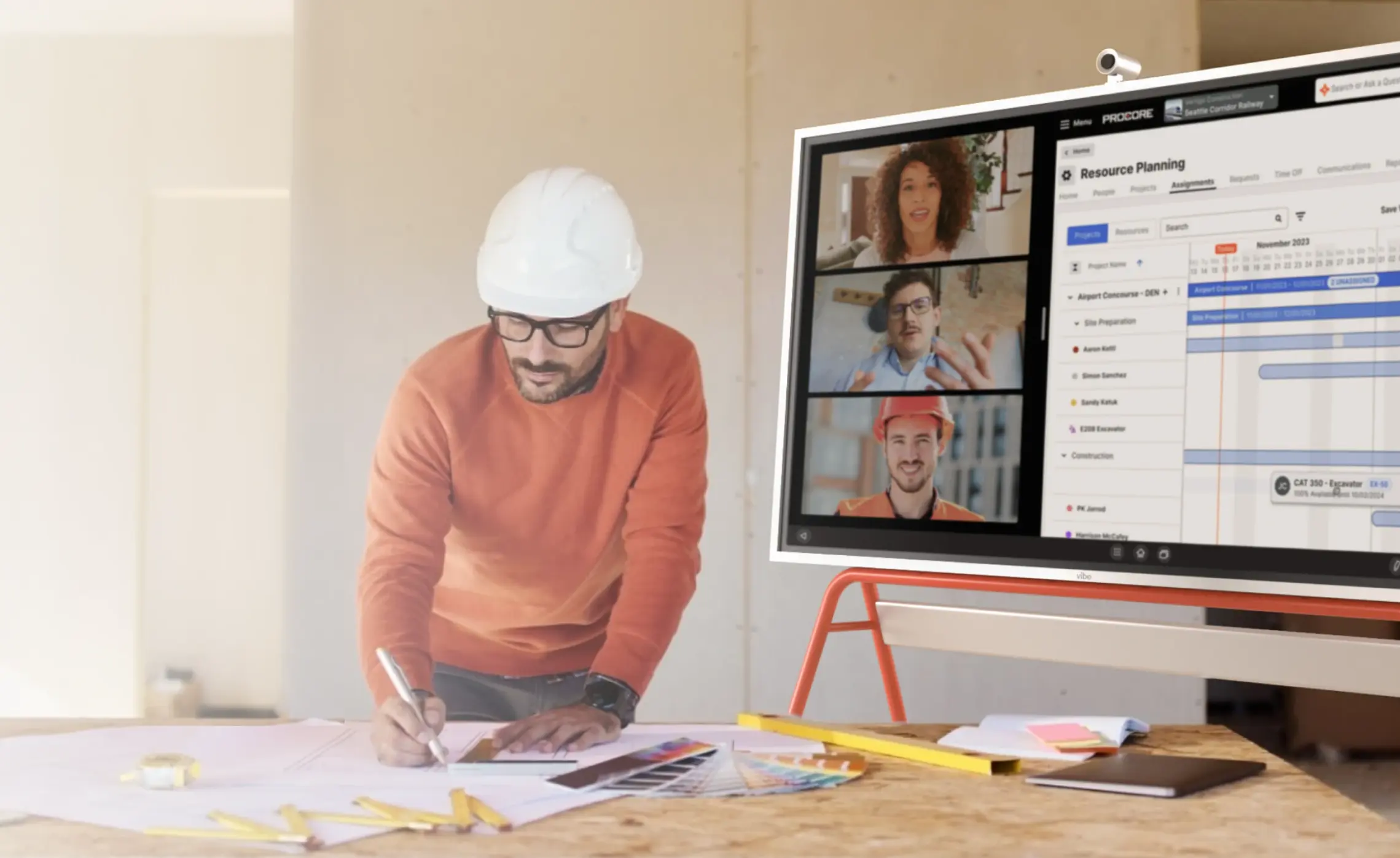 Construction worker reviewing blueprints on a jobsite table beside a Vibe Board S1 Pro displaying a Procore project dashboard and video call